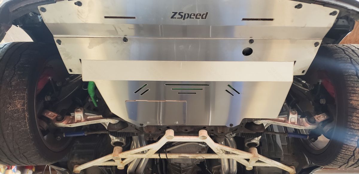 ZSpeed aluminum splash shield under the front of the black 350Z, with the white aftermarket subframe brace below it