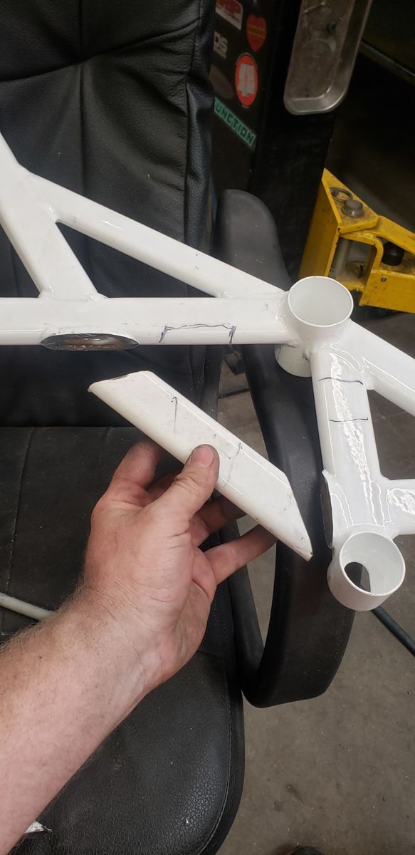 White subframe brace with one leg cut off, held in hand